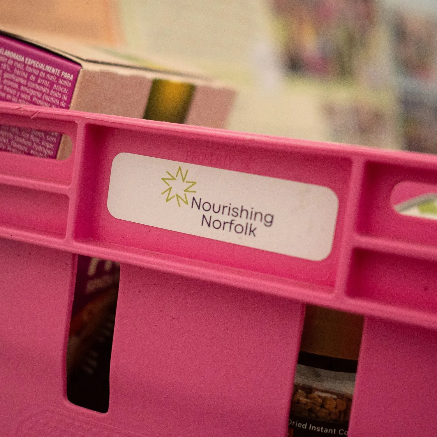 A pink crate full of food with a Nourishing Norfolk sticker on the side
