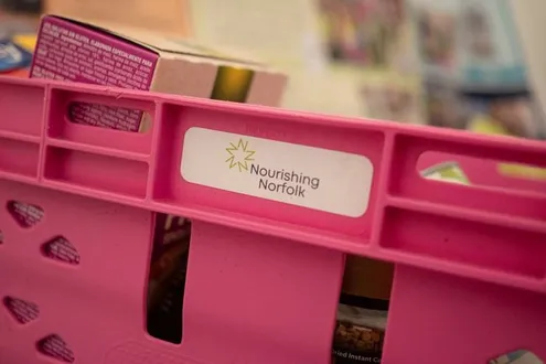 A pink crate full of food with a Nourishing Norfolk sticker on the side